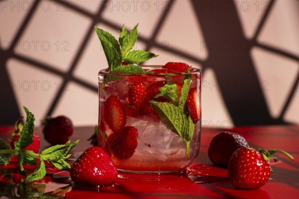 A refreshing strawberry mojito with fresh strawberries and mint, served in a clear glass with ice. On a red surface against a pink background, enhancing the cocktail's vivid colors