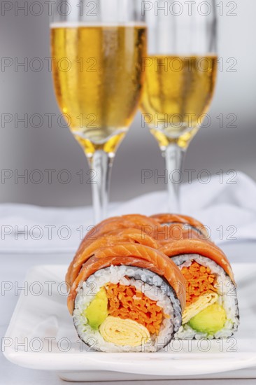 Delicious sushi rolls with salmon, avocado, and omelette are elegantly displayed on a plate, complemented by two sparkling wines in the white background, creating a gourmet dining scene