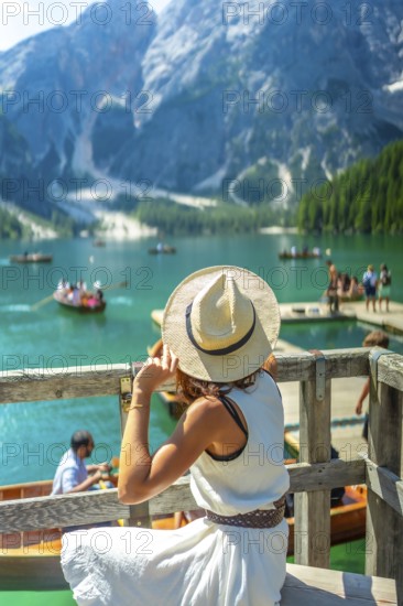 Tourist wearing summer hat looking at lake braies, also called pragser wildsee, with boats and tourists in the dolomites, south tyrol, italian alps, in summer