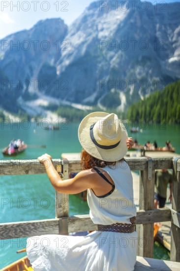 Woman wearing straw hat admiring scenic landscape of lake braies with boats and turquoise water in dolomites, italy