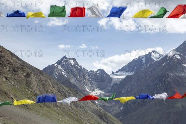 Colorful prayer flags flutter in the foreground, set against the breathtaking backdrop of the majestic mountains in Spiti Valley, India, under a bright blue sky