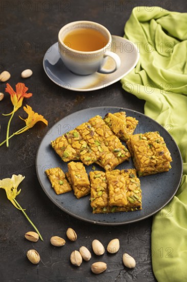 Traditional iranian dessert sohan with cup of green tea on a black concrete background and green textile. side view, close up
