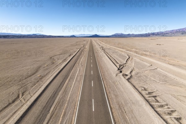 A straight road stretches across a vast desert landscape of the argentine Puna, leading into distant mountains under a clear blue sky, evoking a sense of freedom and adventure