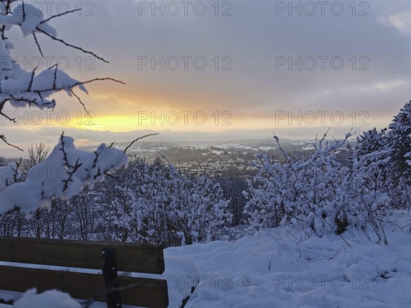 Snowy bench at an orange sunset with a view of Kronach, Frankenwald nature park Park