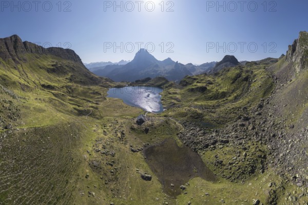 A stunning aerial view captures the tranquil Ayous Refuge surrounded by lush green landscapes and a pristine lake in the heart of the French Pyrenees under a clear blue sky