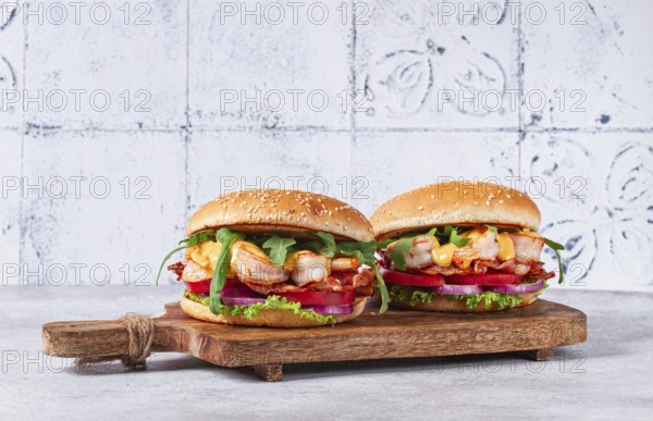 Two shrimp burgers and buns with sesame seeds, bacon, lettuce, tomatoes and onions, On a wooden board