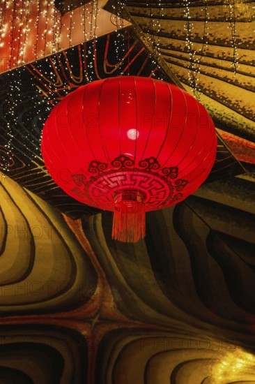 A vivid red lantern adorned with intricate patterns hangs in the festive atmosphere of a Taoist and Chinese Buddhist temple in Macau, illuminated by twinkling lights