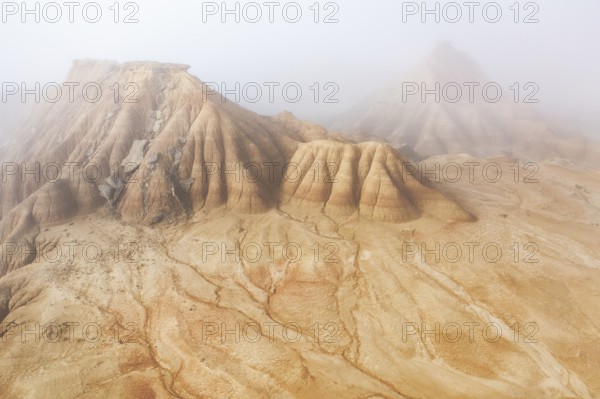 Aerial view of rugged desert formations enveloped in mist Erosion patterns are visible on the sandy surface, creating a mysterious and surreal atmosphere
