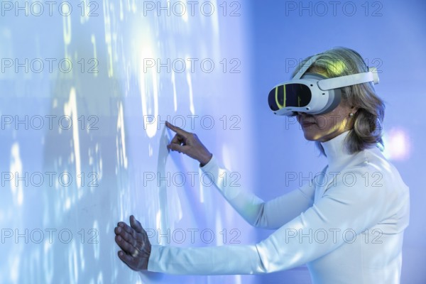 An elderly Asian woman interacts with a virtual environment, wearing a VR headset. She engages with holographic data, illustrating technology's role in connecting generations