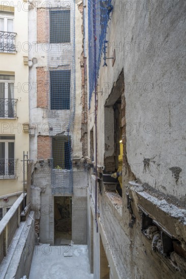 Urban building renovation site with exposed concrete and brick walls. Blue safety nets secure open areas. Visible scaffolding and construction tools indicate work in progress