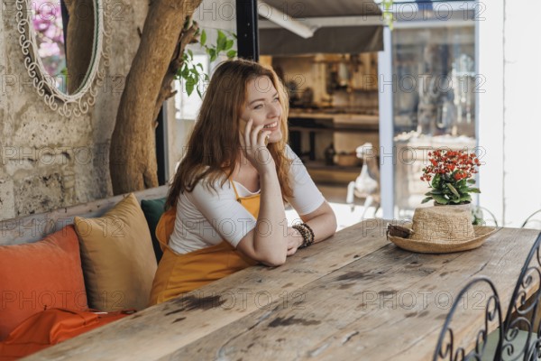 A mature woman, wearing an orange and yellow outfit, enjoys a phone call during her vacation in an old city in Turkey, showcasing a relaxed travel moment