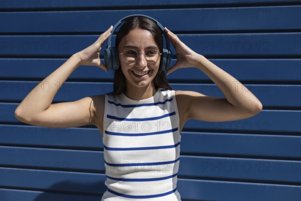 A young woman wearing headphones smiles joyfully while enjoying music in the city outdoors. She embodies a modern, active lifestyle amidst an urban backdrop