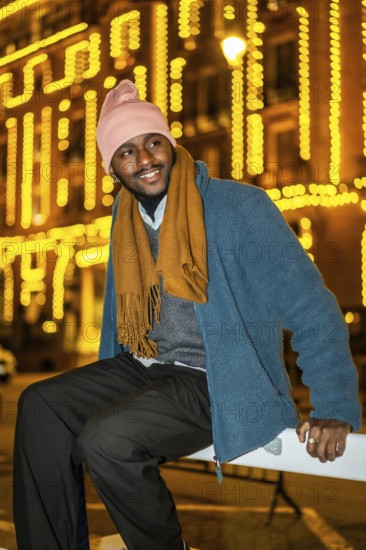 Vertical portrait of an african man sitting outdoors in a Christmas night in the city