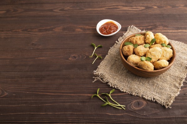 Fried crispy Chicken Nuggets with ketchup, microgreen on brown wooden background and linen textile. side view, copy space