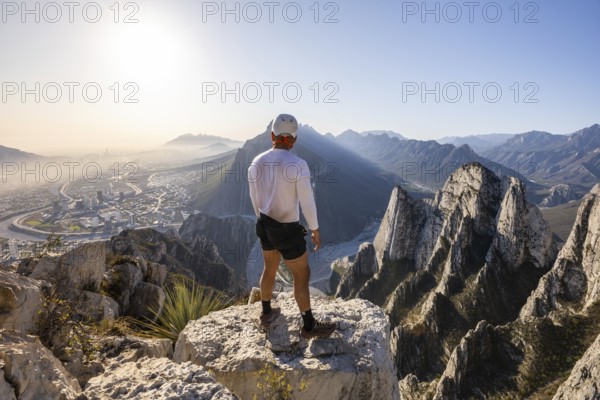 A man stands on a rocky peak at Eagle's Nest in Monterrey, Mexico, taking in the breathtaking view after a day of mountaineering and rappelling. The city and mountains stretch below