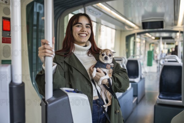 A woman smiles while holding her small chihuahua on a tram. The chihuahua looks calmly at the camera. The scene captures a joyful moment during a pets allowed journey