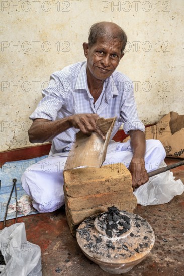 Elderly man works with bricks and coal in traditional clothes, a man burns sapphires in a small oven in the town of Ratnapura in Sri Lanka