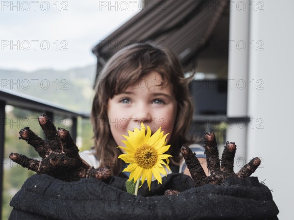 A smiling young girl shows off a bright sunflower and her dirty hands after gardening, capturing a moment of innocent joy and connection with nature
