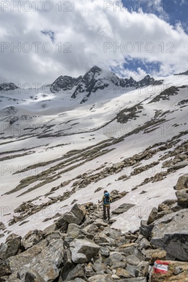 Mountaineer on a hiking trail between snow, descent from the summit of Schönbichler Horn, view of snow-covered and glaciated mountain landscape with summit Großer Möseler, Berliner Höhenweg, Zillertal Alps, Tyrol, Austria