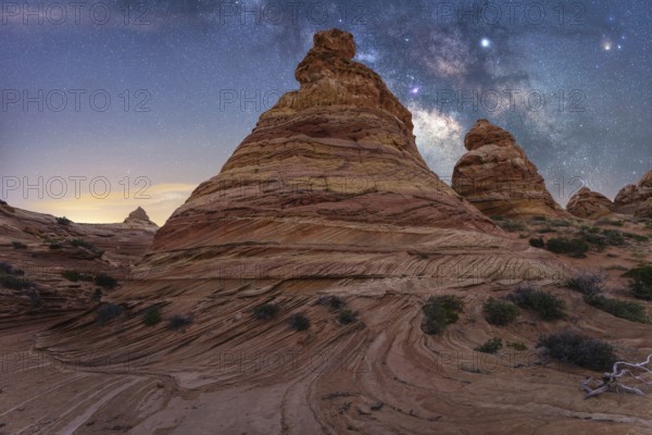 Scenic view of striking rock formations with swirling patterns under a mesmerizing starry night sky, showcasing the beauty of nature artistry and cosmic wonder in Coyote Buttes, Arizona