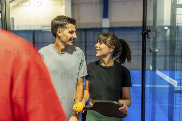 Two smiling adult players holding a paddle and ball, sharing a moment during a friendly pickleball match, representing an active lifestyle and leisure activity