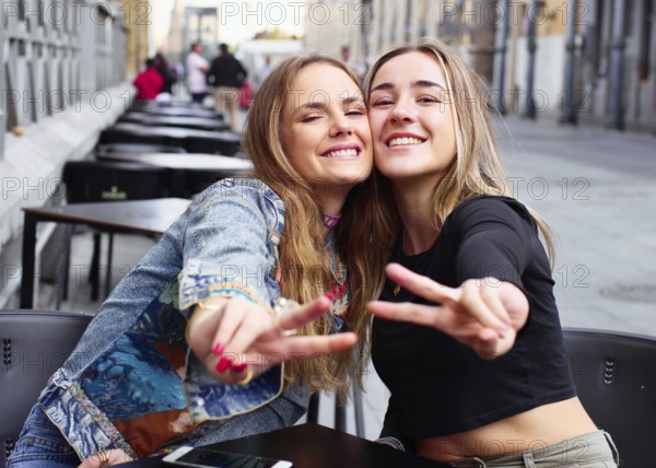 Two cheerful teenage friends enjoying time together outdoors, smiling and posing with peace signs. Capturing a fun and carefree moment in an urban setting
