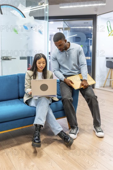Two young professionals working together, sharing ideas and using a laptop in a modern coworking office space