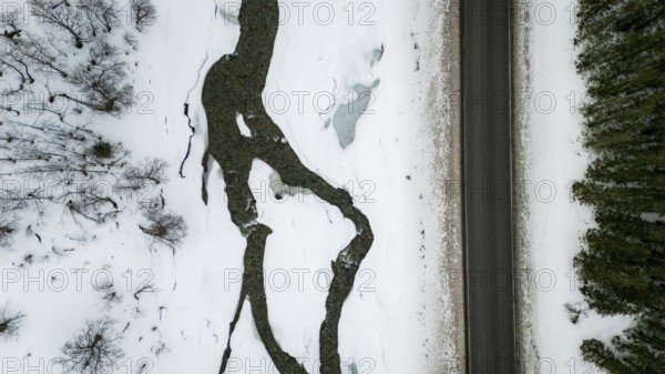 Aerial view of a Nordic landscape showcasing a road flanked by a frozen stream and snow-laden trees. The serene winter scene captures nature's tranquil beauty, Bardu, Troms, Norway