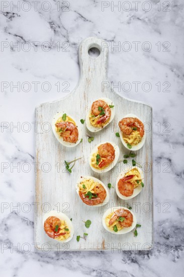 Boiled eggs stuffed with yolk and seasoned with mayonnaise, stuffed eggs with shrimp, on a white wooden chopping board, selective focus, close-up, without people