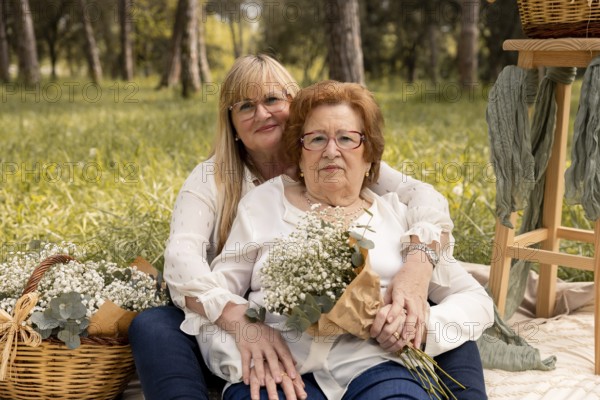 An affectionate mother and daughter pair sit in an idyllic grassy field, surrounded by nature's beauty, sharing an intimate moment of connection and joy. Baskets with flowers add a charming touch