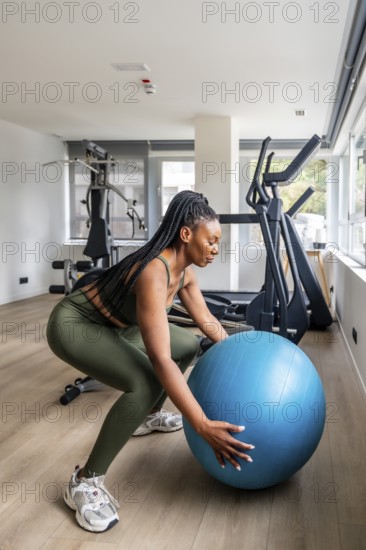Businesswoman maintaining her workout routine while traveling, performing squats with a fitness ball in a hotel gym