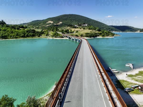 A breathtaking view of a bridge extending over a turquoise lake surrounded by lush hills in Italy, capturing the picturesque charm and serene beauty of Italian nature