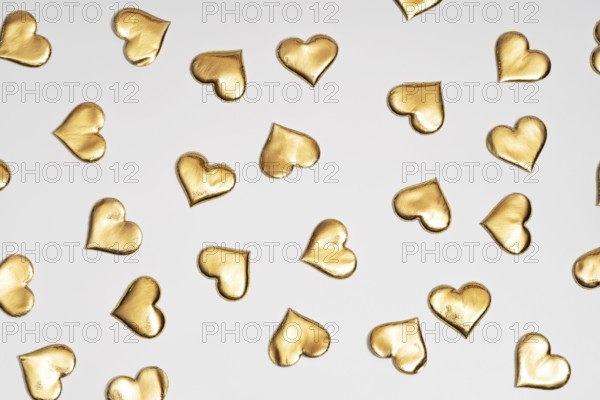 Numerous golden heart shapes artistically arranged on a plain white surface, symbolizing love and St. Valentine's Day. Ideal for themes related to romance and special occasions