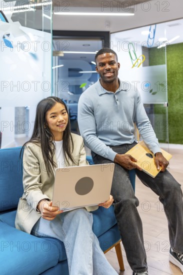 Two smiling business people holding a laptop and a tablet in a modern coworking office, showcasing teamwork and collaboration