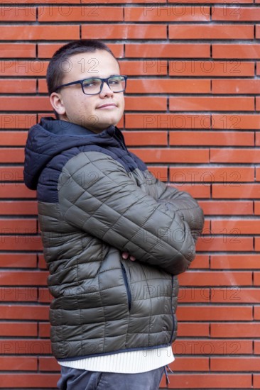 A young man with an intellectual disability stands confidently with arms crossed against a brick wall