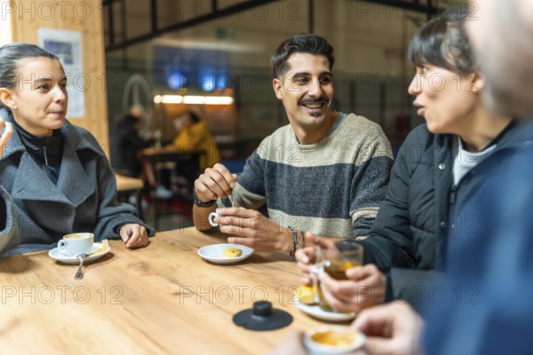 Diverse group of friends socializes and talks while drinking coffee and tea at a wooden table in an indoor cafe setting, building community after a pickleball game