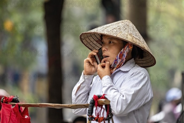 Woman with traditional straw hat making a phone call outdoors, A woman talking on the phone in the streets of Hanoi Vietnam