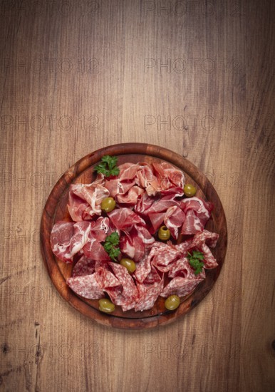 Assortment, sliced meat appetizer, prosciutto, salami and ham, with olives, on a wooden board, breakfast, top view, close-up, no people