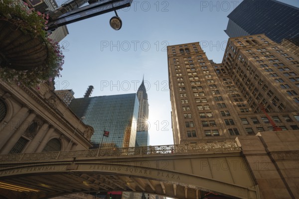 From below the morning view of Pershing Square Plaza in front of Grand Central Terminal with the iconic Chrysler Building and modern skyscrapers in Manhattan, New York City. The soft sunlight enhances the majestic urban scenery