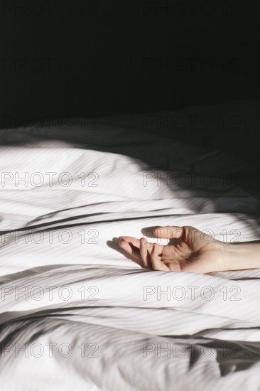 A serene hotel room captured at dawn, where soft morning light filters through, casting gentle shadows on a crisp white bed. An outstretched hand adds a touch of mystery