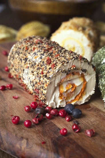 Close-up image of a spiced cheese roll coated with mixed herbs and peppercorns, accented with scattered berries on a rustic wooden table