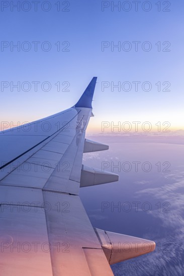A serene view from an airplane window showcasing the wing against a backdrop of a stunning sunrise and clear blue sky, capturing the essence of air travel and adventure