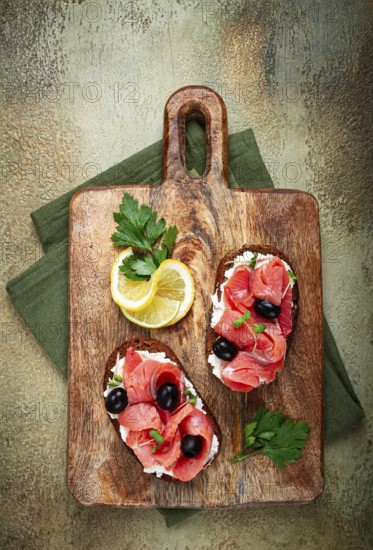 Sandwiches with cream cheese, chum salmon, cold smoked, grain bread, on a cutting board, top view, breakfast, lemon and parsley, no people