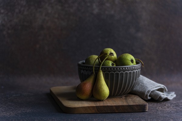 A rustic display of fresh wild pears in a textured ceramic bowl sitting atop a wooden surface creates a natural, earthy vibe. Perfect for culinary or nature themed projects