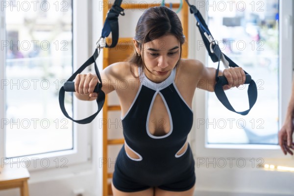 Woman using suspension straps for trx style physiotherapy, focusing on strength and rehabilitation during a clinical exercise session for recovery and functional fitness