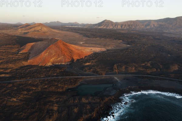Aerial shot showcasing the stunning juxtaposition of Timanfaya national park and Los Hervideros against the dark volcanic terrain, under the golden hour light