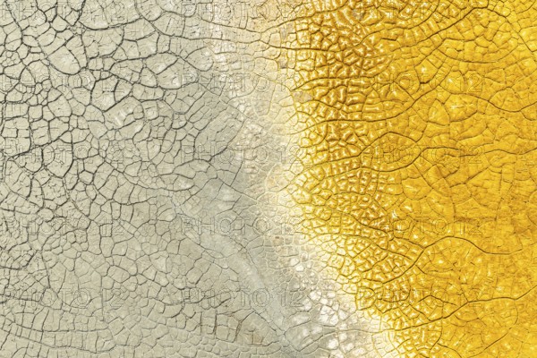 A close-up of cracked mud with striking multicolor patterns, featuring vivid yellow on one side and muted grey on the other The texture captures natural earth details