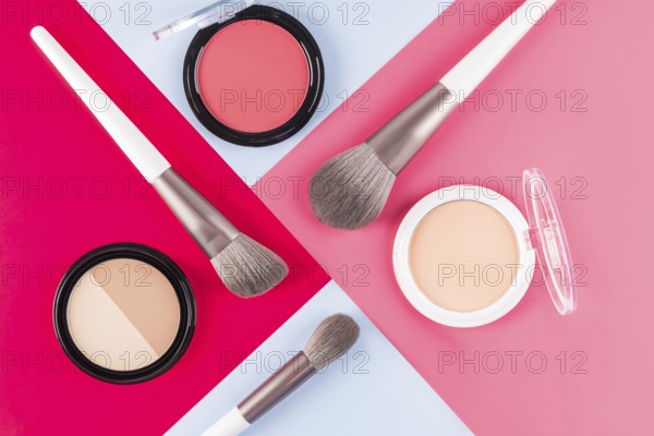 Aesthetic arrangement of makeup brushes and powder compacts on contrasting red, pink and blue surfaces. Perfect for beauty, fashion, and cosmetic themed designs