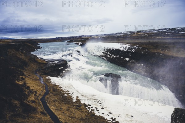 Stunning view of Gullfoss waterfall, cascading powerfully over rugged cliffs. The icy landscape and flowing water create a mesmerizing natural spectacle in Iceland