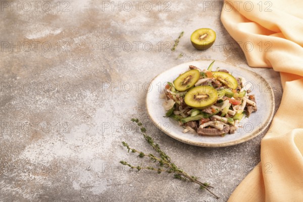 Meat salad with beef kiwi and vegetables on brown concrete background and orange linen textile. side view, copy space